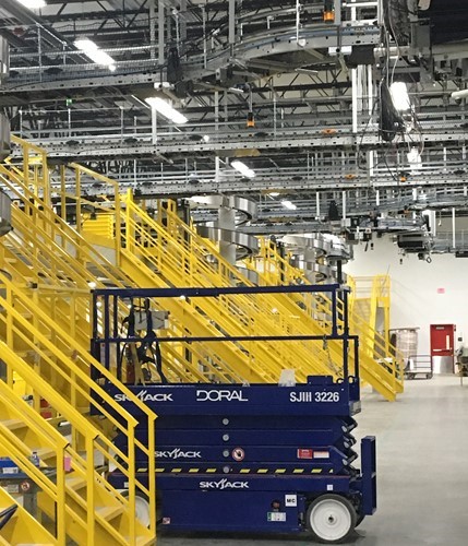 A Doral lift near yellow metal staircases and railings leading up to a mezzanine in a plant