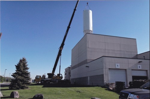 The outside of a plant where a crane is handling a silo into a roof opening