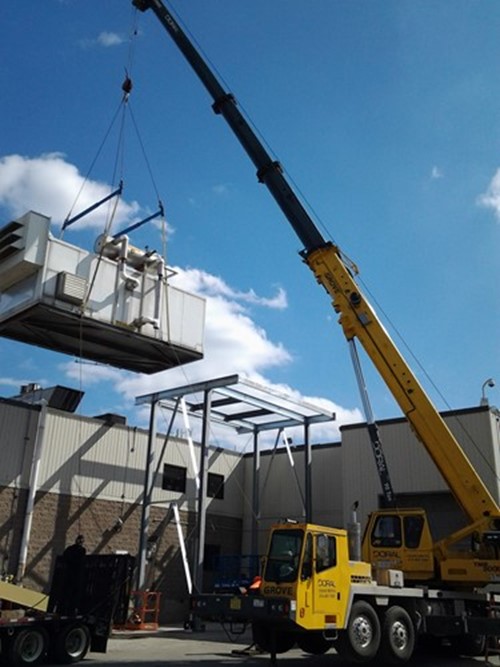 A large crane lifting and setting a chiller outside of a plant